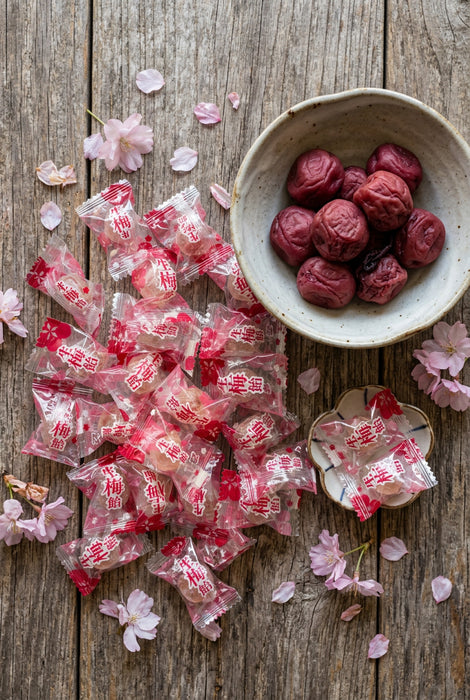 Pink individually wrapped candies on a table next to a bowl with japanese umeboshi