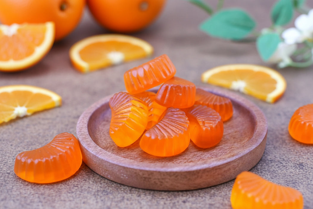 Orange gummy candies on a wooden plate with orange slices in the background
