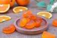 Orange gummy candies on a wooden plate with orange slices in the background