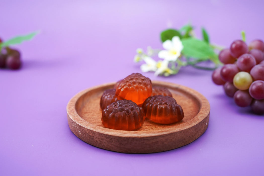 Gummy grapes on a wooden plate with a purple background and flowers.