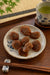 A plate of seedless sweet and sour ume on a Japanese plate with chopsticks on the side and a cup of green tea in the background. 