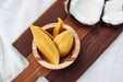 Yellow pickled mango on wooden board with coconut open in the background
