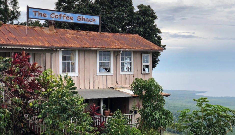 Wooden building with 'The Coffee Shack' sign, surrounded by greenery and overlooking a scenic landscape.