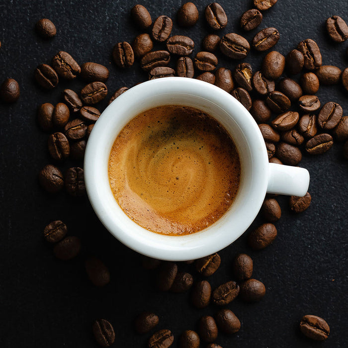 White cup of espresso surrounded by coffee beans on a dark surface