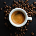 White cup of espresso surrounded by coffee beans on a dark surface